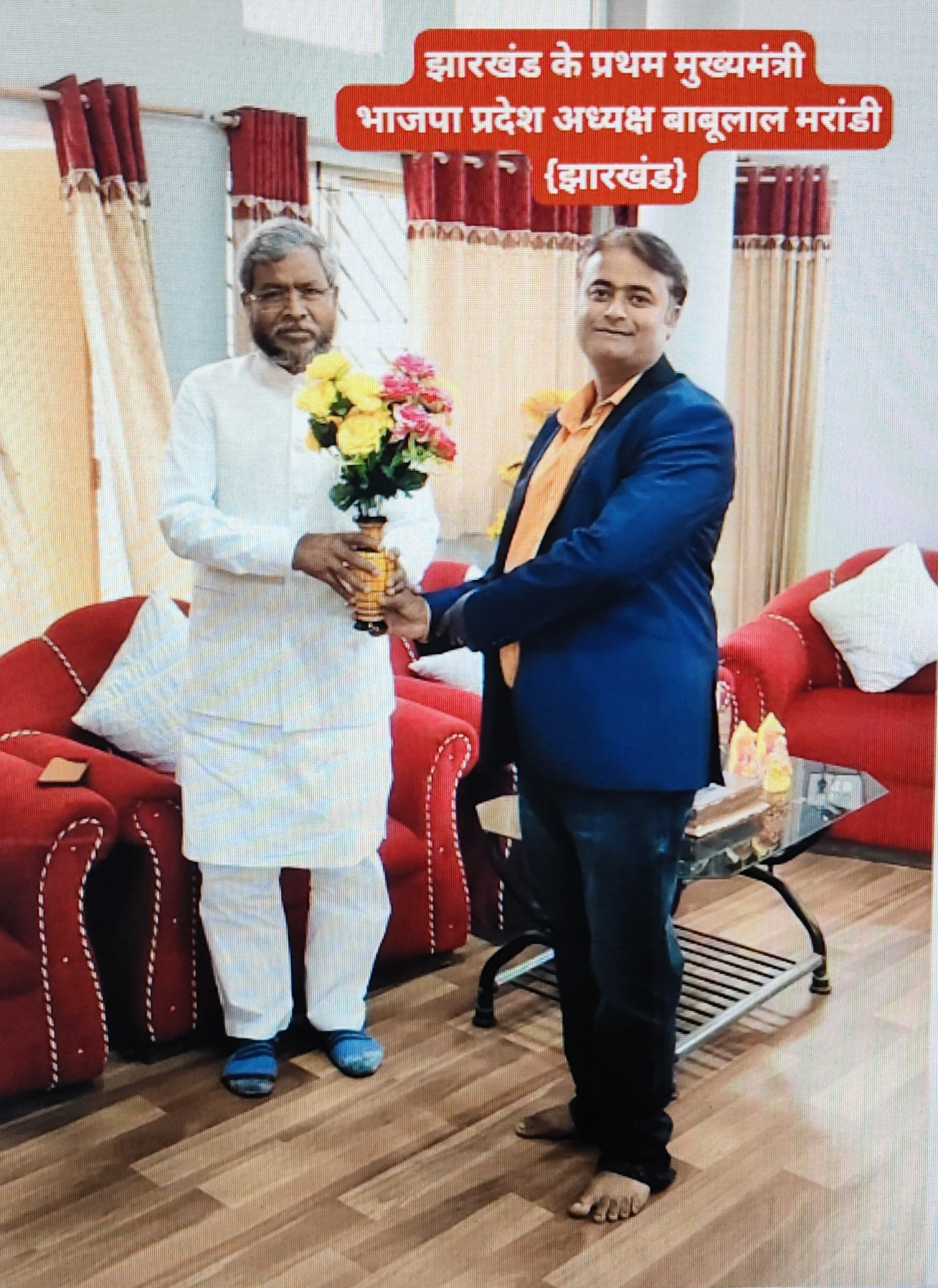 A man in a blue suit standing next to Babulal Marandi holding flowers
